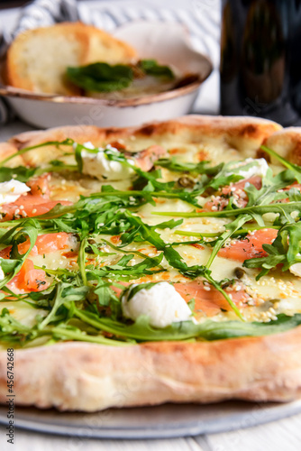 Pizza with mozzarella, salmon slices, fresh arugula. Served with baked cheese camembert and red wine. Italian cuisine