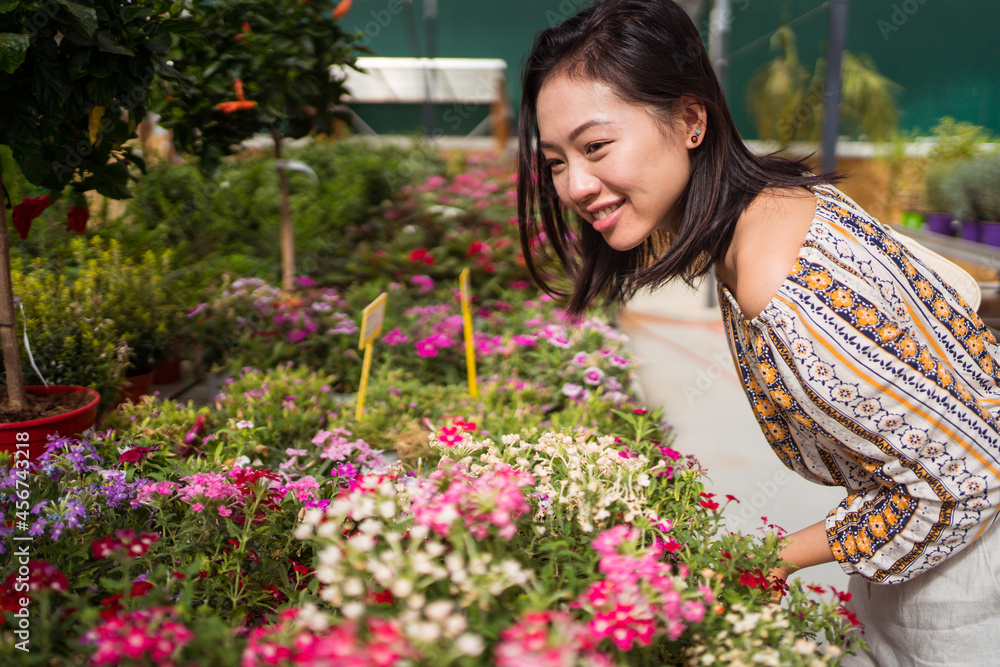 Smiling Asian buyer choosing blooming flowers in garden shop Smiling Asian buyer choosing blooming flowers in garden shop