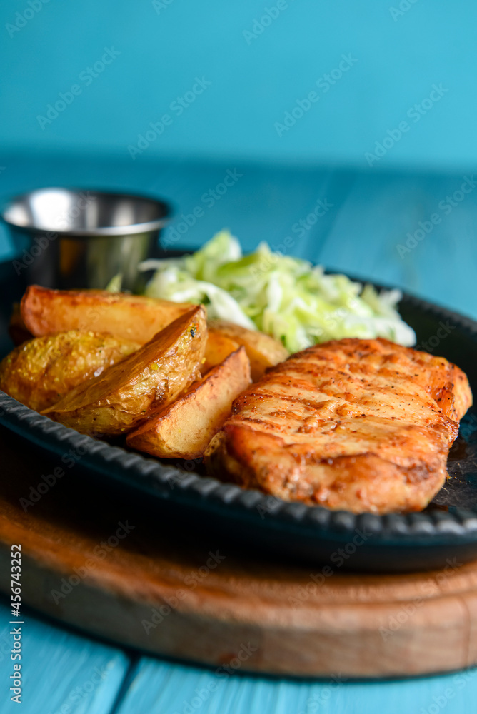 Grilled Chicken Steak with fried potatoes in rural style and coleslaw salad served in a tray over blue background.