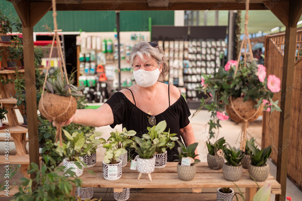 Buyer in fabric mask choosing plants in garden shop Buyer in fabric mask choosing plants in garden shop