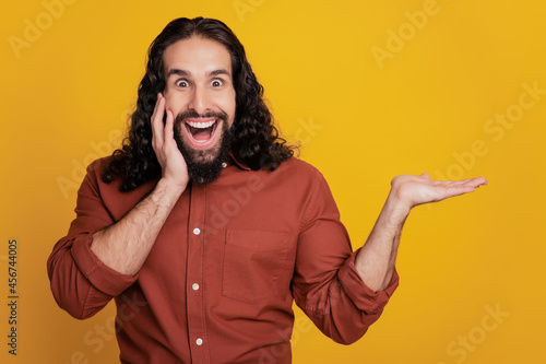 Portrait of excited promoter guy palm cheek hold object empty space on yellow background