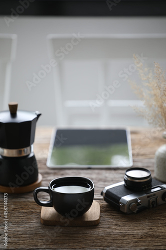 Black coffee cup and black moka pot with camera and tablet on wooden table