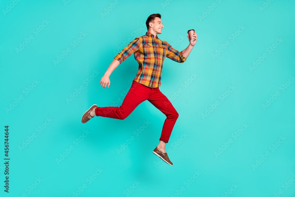 Full length profile photo of funny brunet millennial guy jump hold coffee wear shirt turquoise sneakers isolated on teal background