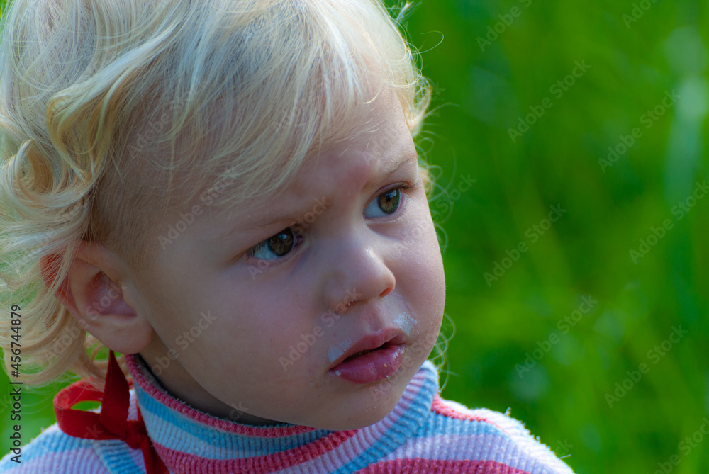 A blond-haired blond boy in a striped blouse and with a face smeared with cream, attentively and intently looks at something close-up A blond-haired blond boy in a striped blouse and with a face smeared with cream, attentively and intently looks at something close-up