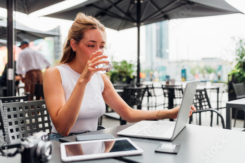 Young flexible worker business woman remote working sitting bar drinking water photo