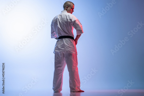 Back view full-length portrait of young sportsman in white kimoto isolated over gradient white blue background. Karate, judo, taekwondo sport photo