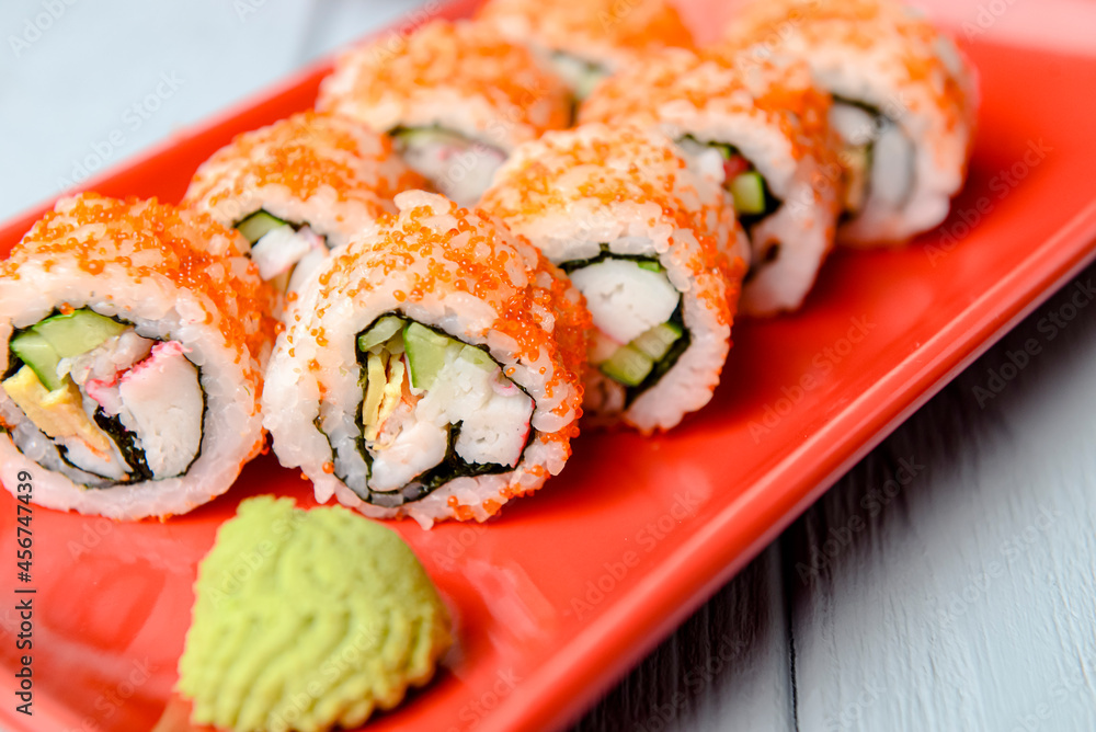 California sushi rolls served on a red plate over light wooden background. Close up, selective focus on sushi. California sushi rolls served on a red plate over light wooden background. Close up, selective focus on sushi.