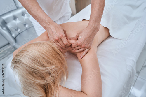 Beauty salon customer having her shoulder massaged by a massotherapist