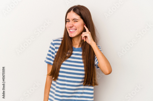 Young caucasian woman isolated on white background covering ears with fingers, stressed and desperate by a loudly ambient. © Asier