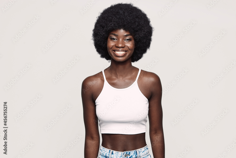 Beautiful young African woman looking at camera and smiling while standing against gray background Beautiful young African woman looking at camera and smiling while standing against gray background