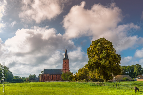 Drenthe landscape with Gothic Jacobus church and bell tower built in the 15th century in Rolde in the Dutch province of Drenthe with a meadow against a sky with cumulus clouds