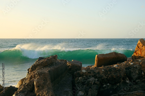 A wave, pierced by the light of the sunset, runs over the stones.