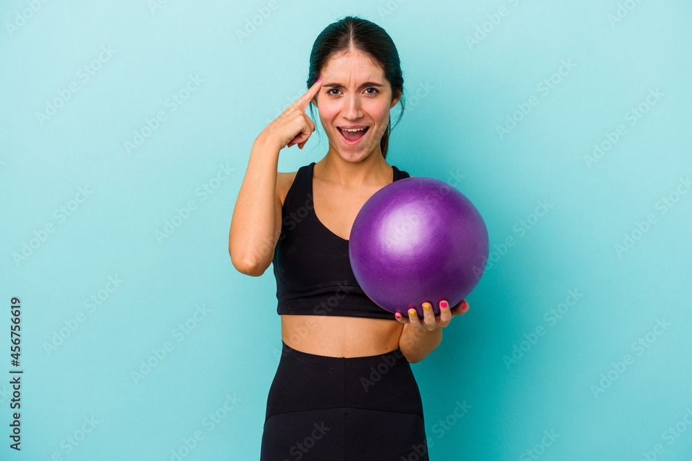 Young caucasian fitness woman holding a ball isolated on blue background showing a disappointment gesture with forefinger.