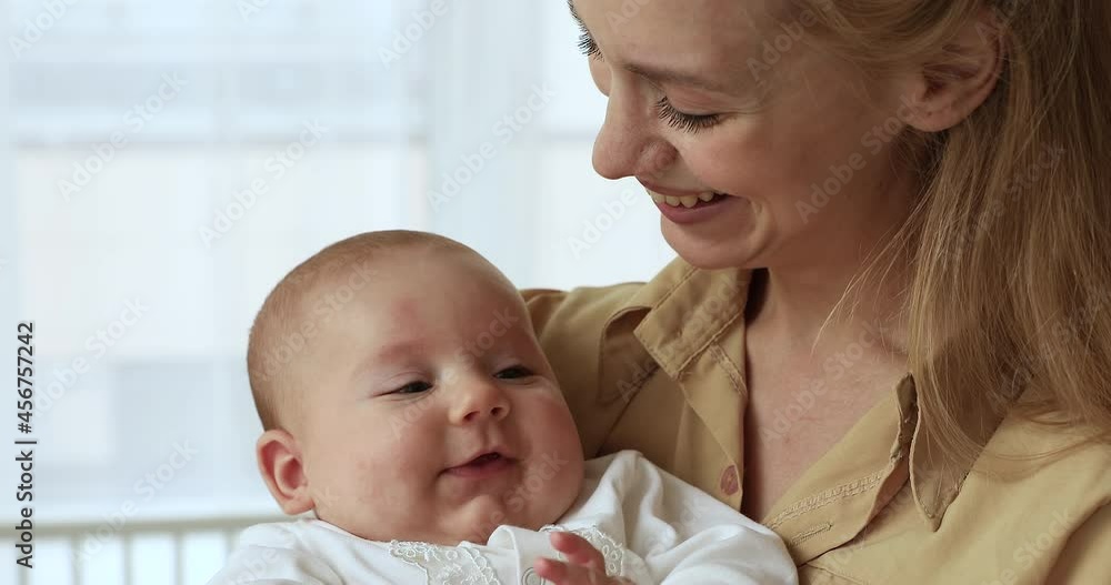 Loving young 25s mother holding on hands adorable infant baby, caring mom sings a song or lullaby for daytime healthy nap, close up. Happy motherhood, sweet tender moments of parent and child concept Loving young 25s mother holding on hands adorable infant baby, caring mom sings a song or lullaby for daytime healthy nap, close up. Happy motherhood, sweet tender moments of parent and child concept
