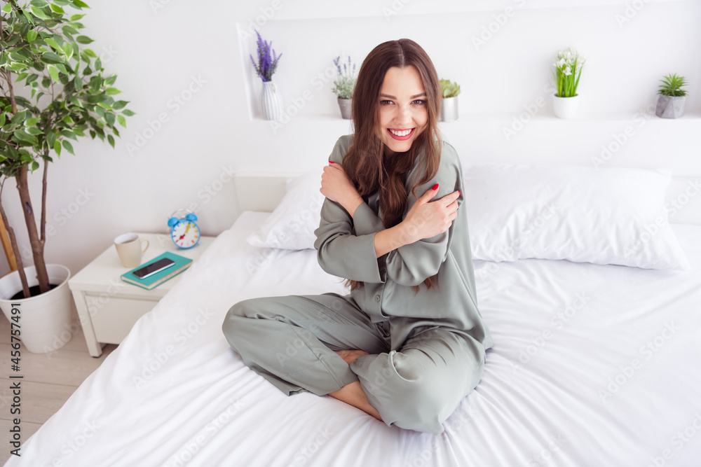 Portrait of attractive cheerful girl sitting on bed hugging herself sweet day at home house light white interior Portrait of attractive cheerful girl sitting on bed hugging herself sweet day at home house light white interior