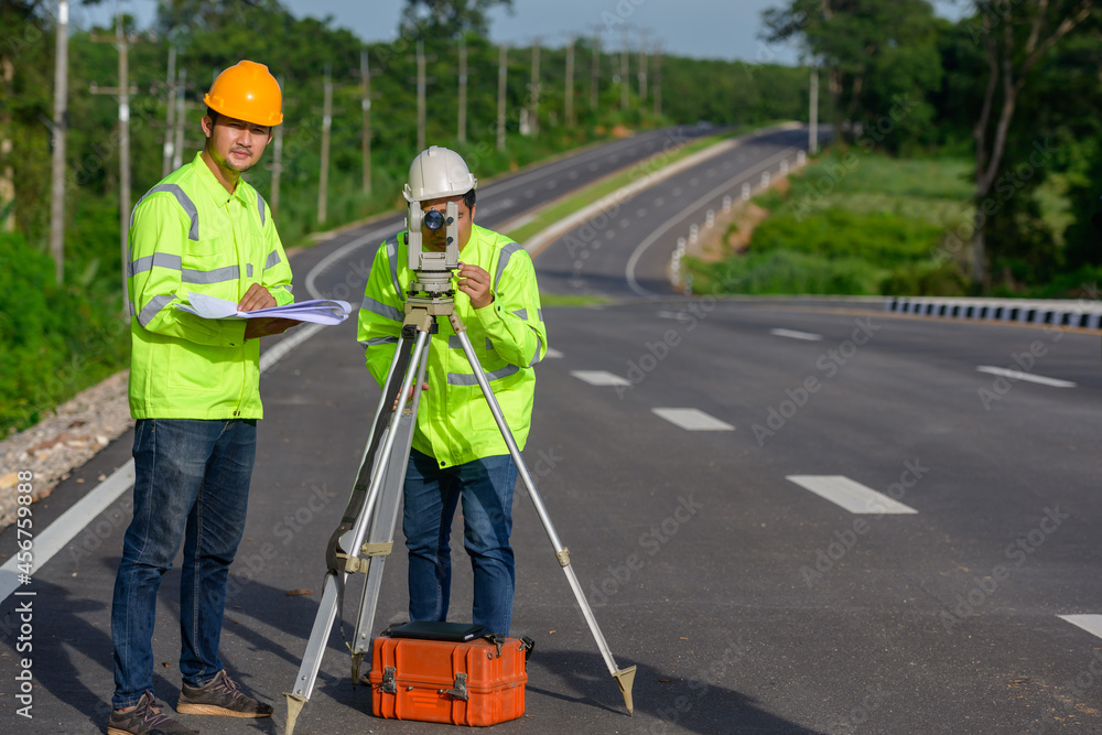 Picture of two civil engineers using theodolites measuring land coordinates standing at outdoor theodolites at a road construction site. Picture of two civil engineers using theodolites measuring land coordinates standing at outdoor theodolites at a road construction site.
