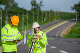 Picture of two civil engineers using theodolites measuring land coordinates standing at outdoor theodolites at a road construction site.