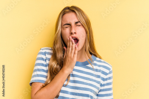 Young caucasian blonde woman isolated on yellow background yawning showing a tired gesture covering mouth with hand.