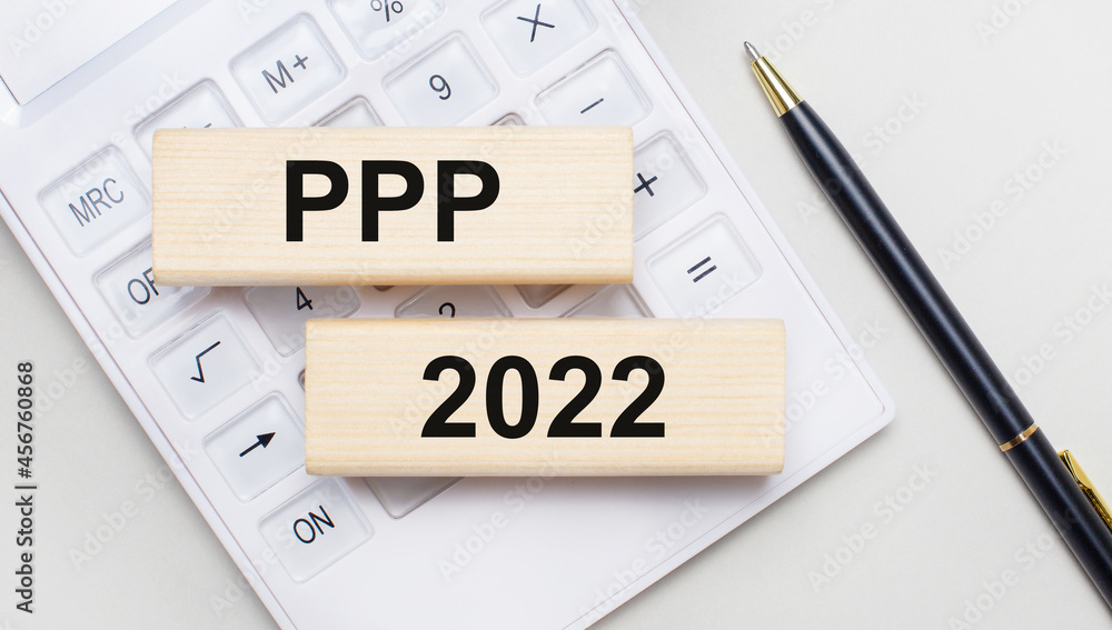 Wooden blocks with the text PPP 2022 lie on a light background on a white calculator. Nearby is a black handle. Business concept Wooden blocks with the text PPP 2022 lie on a light background on a white calculator. Nearby is a black handle. Business concept