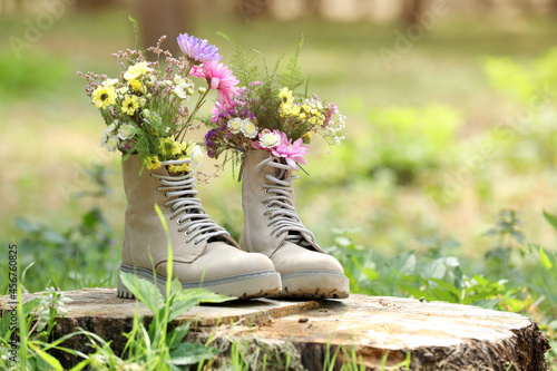 Beautiful flowers in boots on stump outdoors, space for text photo