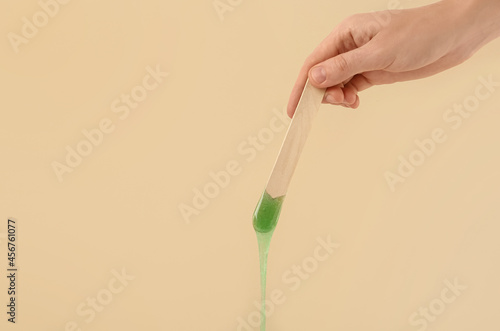 Woman holding spatula with hot depilatory wax on beige background, closeup. Space for text photo