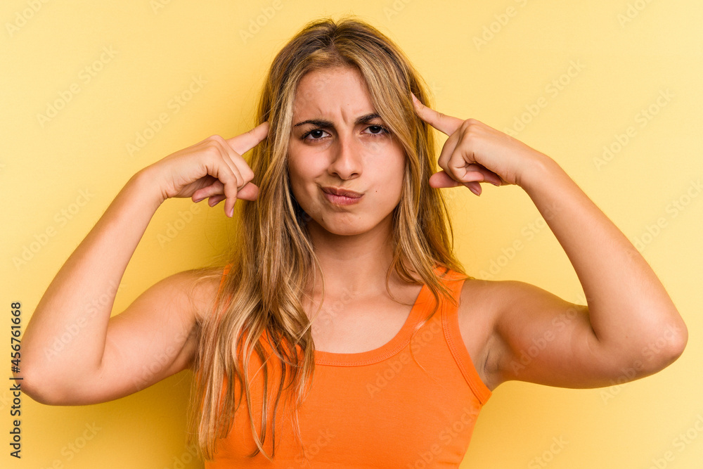 Young caucasian blonde woman isolated on yellow background  focused on a task, keeping forefingers pointing head.