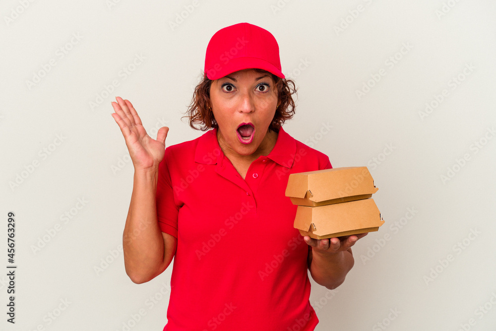 Middle age delivery woman taking burguers isolated on white background surprised and shocked. Middle age delivery woman taking burguers isolated on white background surprised and shocked.