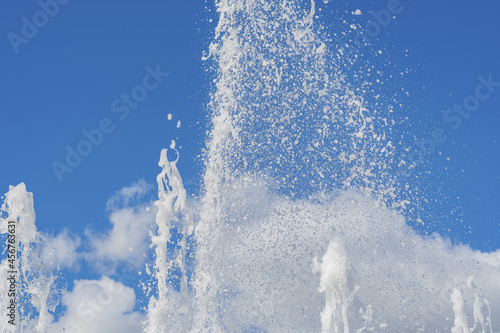 Several vertical streams of water rise up and splatter against the blue cloudy summer sky. photo