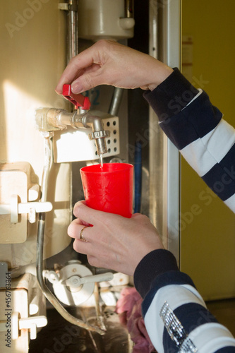 A woman on the train carefully pours boiling water into a red mug.