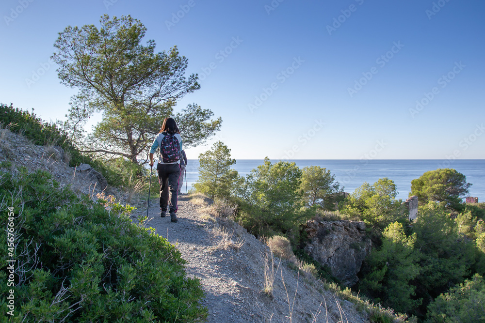 Hiker walking along narrow path that is in a forest by the sea on the cliffs of Maro Cerro Gordo Hiker walking along narrow path that is in a forest by the sea on the cliffs of Maro Cerro Gordo