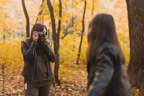 Mother taking picture her charismatic daughter on retro camera in autumn park. Hobbies and leisure concept. © satura_