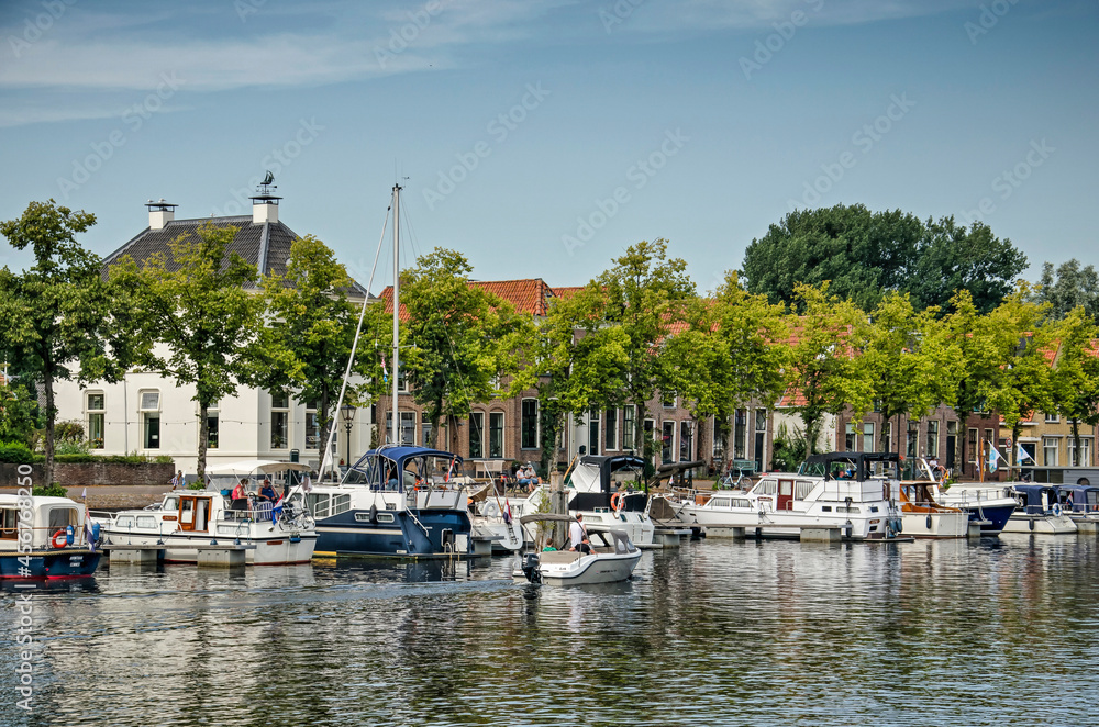 Blokzijl, The Netherlands, August 12, 2021: small yachts and sailboats moored at the old town's harbour, lined with trees and historic brick houses
