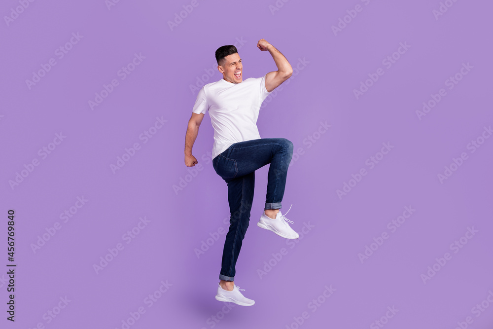 Full size photo of young cheerful crazy man jump up raise fist winner enjoy isolated on violet color background Full size photo of young cheerful crazy man jump up raise fist winner enjoy isolated on violet color background