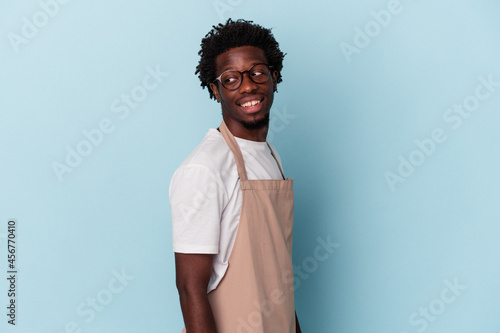 Leinwand Poster Young african american store clerk isolated on blue background looks aside smiling, cheerful and pleasant