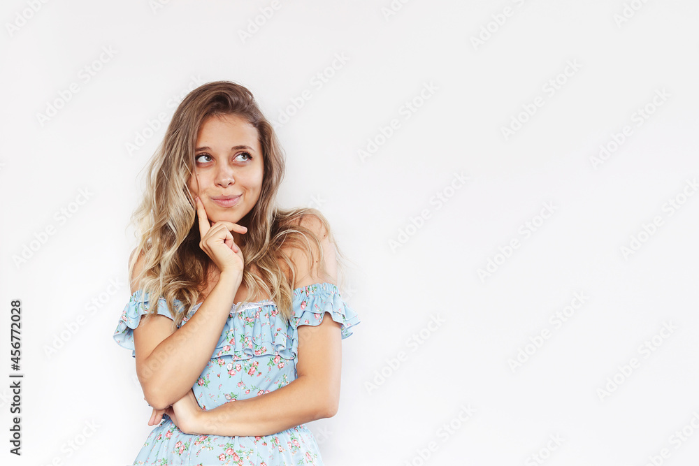 A young caucasian mystery smiling blonde woman with wavy hair in a blue dress imagines or thinks looking up at empty copy space for ads, promo, offer, text, slogan isolated on a white background A young caucasian mystery smiling blonde woman with wavy hair in a blue dress imagines or thinks looking up at empty copy space for ads, promo, offer, text, slogan isolated on a white background