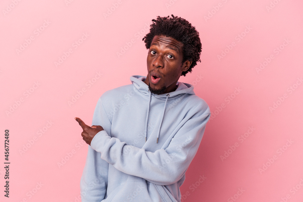 Young african american man isolated on pink background smiling and pointing aside, showing something at blank space. Young african american man isolated on pink background smiling and pointing aside, showing something at blank space.
