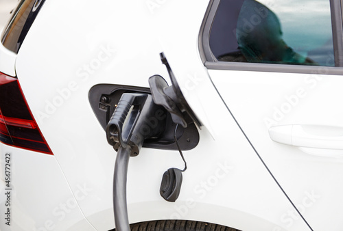 Closeup view of electric car with the power cable supply plugged in charging at the public charging station.