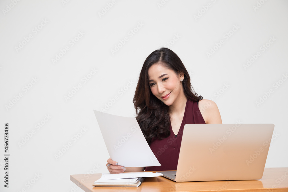 Young Asian woman reading document paper and sitting with computer laptop on wood table Young Asian woman reading document paper and sitting with computer laptop on wood table