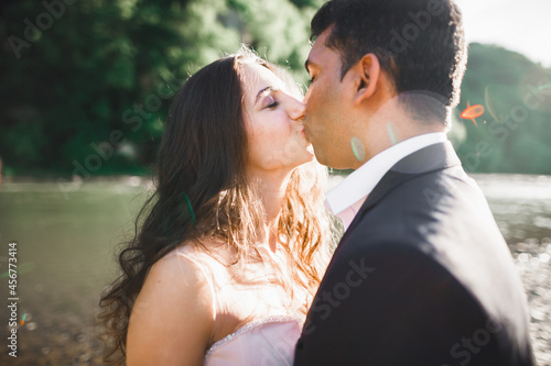Beautifull wedding couple kissing and embracing near the shore of a mountain river with stones © olegparylyak