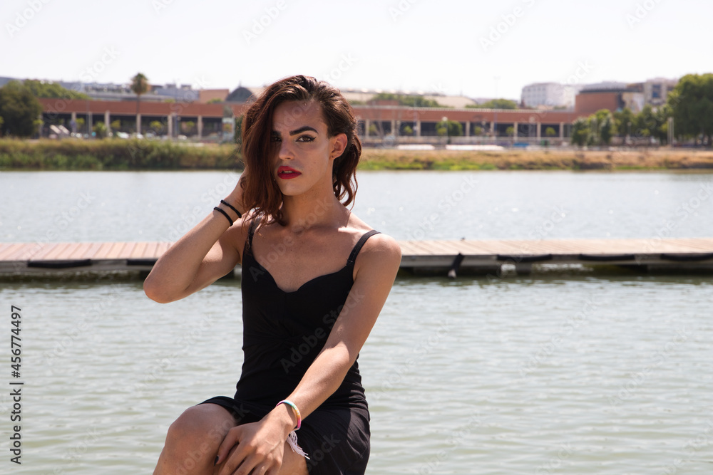 young latina and transsexual woman sitting on the river pier in a black dress. Concept diversity, transgender, and freedom of homosexual expression.