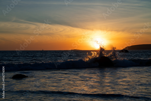 Waves crashing over large beached rocks at sunset in Bodega Bay, CA