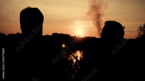 Two young guys smoke a hookah on a sunset background.