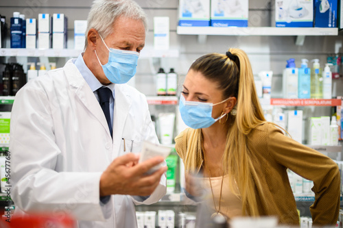 Senior pharmacist dealing with a customer  both of them wearing masks due to coronavirus