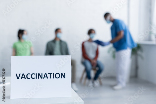 sign plate with vaccination lettering near blurred african american doctor and patients