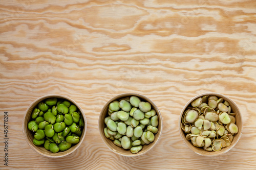 Raw broad beans in bowls. Peeled, unpeeled and separated seed skins of broad beans top view with copy space.