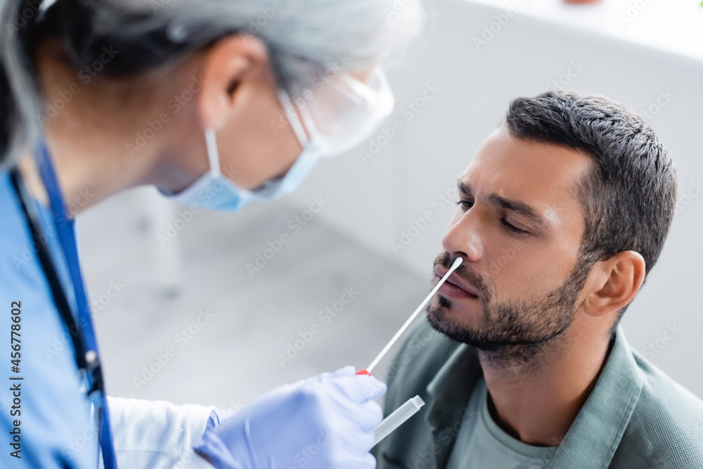 blurred nurse in medical mask taking samples for coronavirus test from young man blurred nurse in medical mask taking samples for coronavirus test from young man