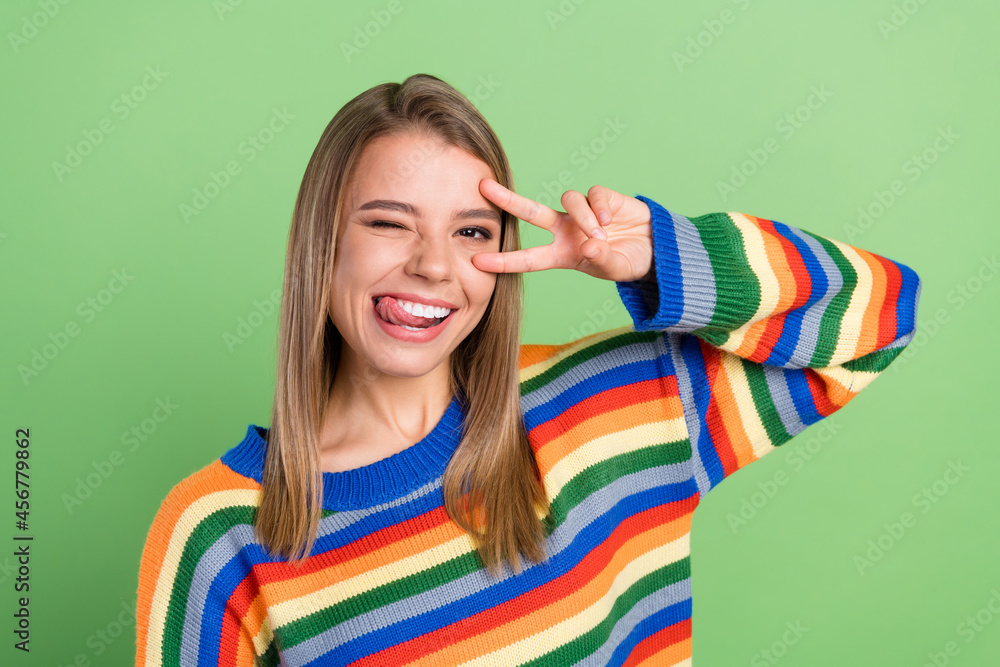 Photo portrait smiling girl showing v-sign gesture licking lips isolated pastel green color background Photo portrait smiling girl showing v-sign gesture licking lips isolated pastel green color background
