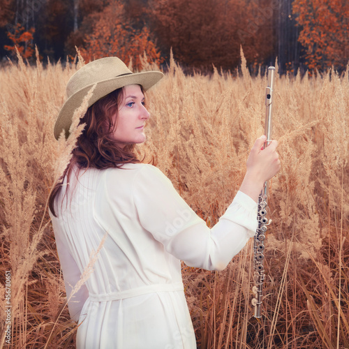 A woman with big flute boehm stands in autumn grass, yellow field photo