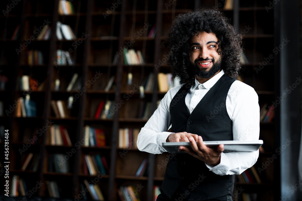 Happy beautiful Egyptian student is preparing for a lecture in the library, holding a book in his hands Happy beautiful Egyptian student is preparing for a lecture in the library, holding a book in his hands