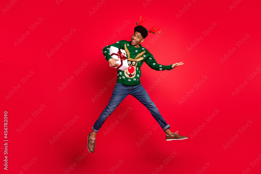Full length body size view of trendy handsome cheerful guy jumping holding gift having fun isolated over vivid red color background